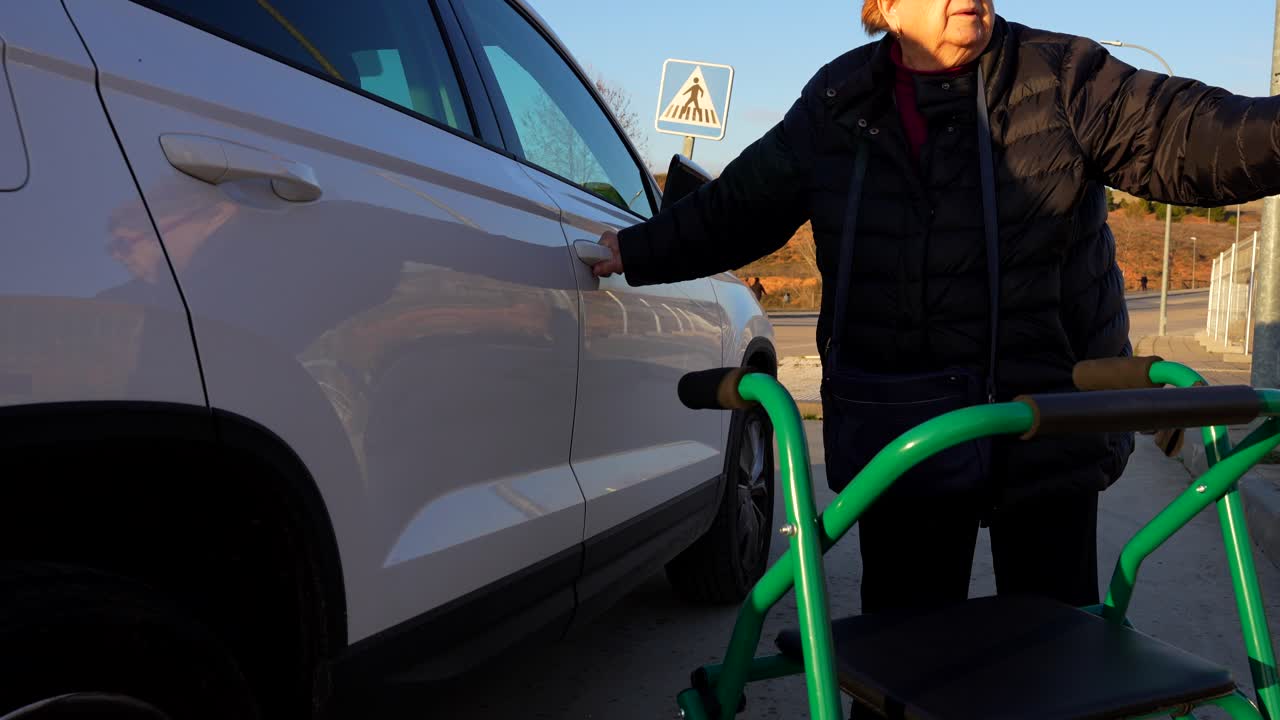 Older woman, aided by a walker, gets to a car and tries to get door open