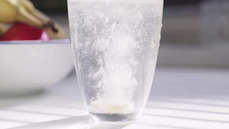 primer plano de una tableta gaseosa cayó en un vaso de agua en un entorno de cocina de la mañana