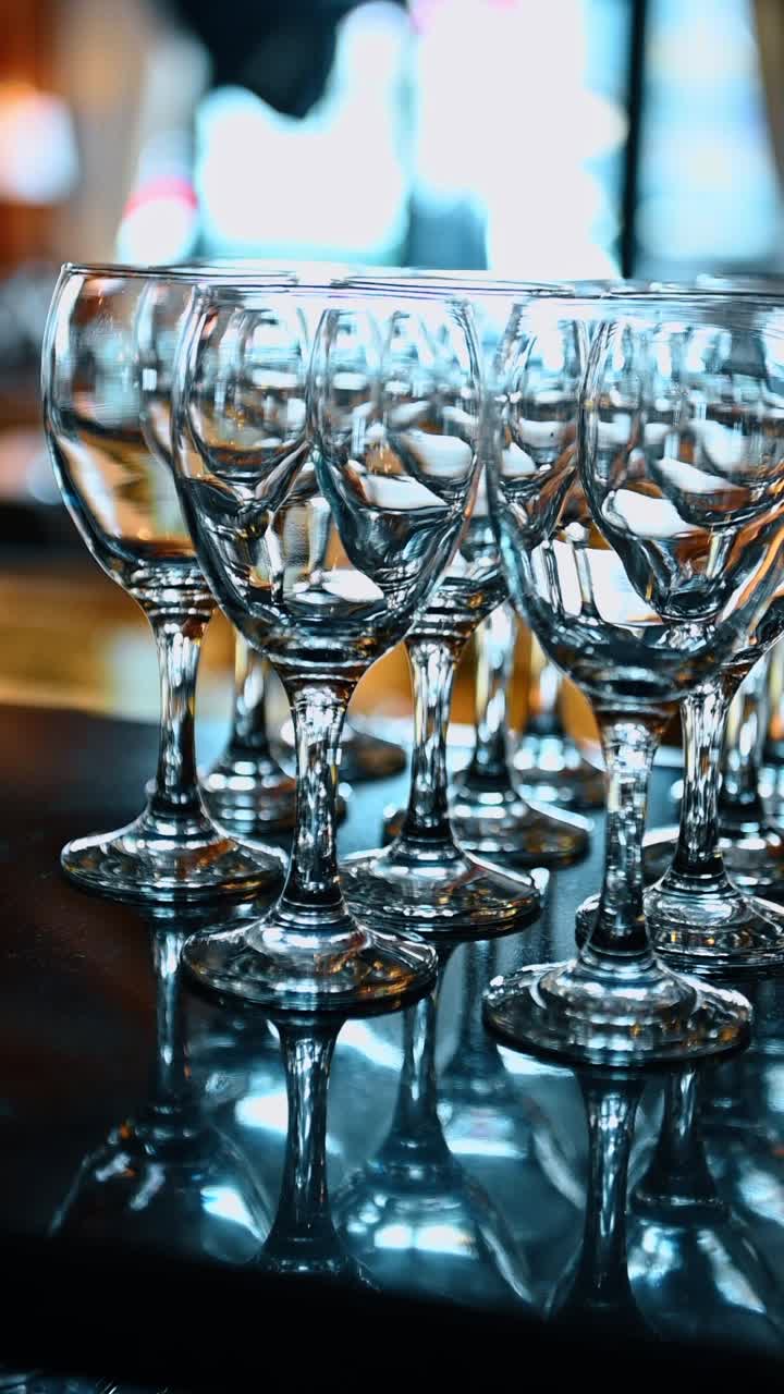 Rækker af tomme, rene vinglas på en mørk reflekterende overflade. Flere klare glas på stilk arrangeret i rækker på et sort bord med refleksioner og bokeh-baggrund.