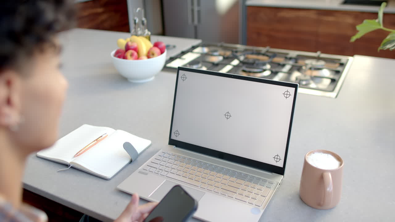 Talking on smartphone, teenage boy working on laptop in modern kitchen with coffee, copy space