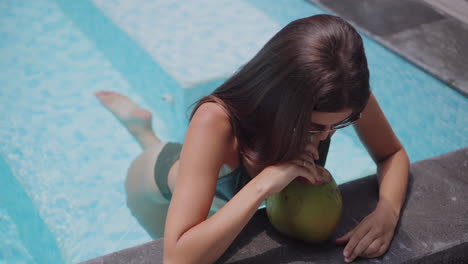 mujer disfrutando de un coco junto a la piscina