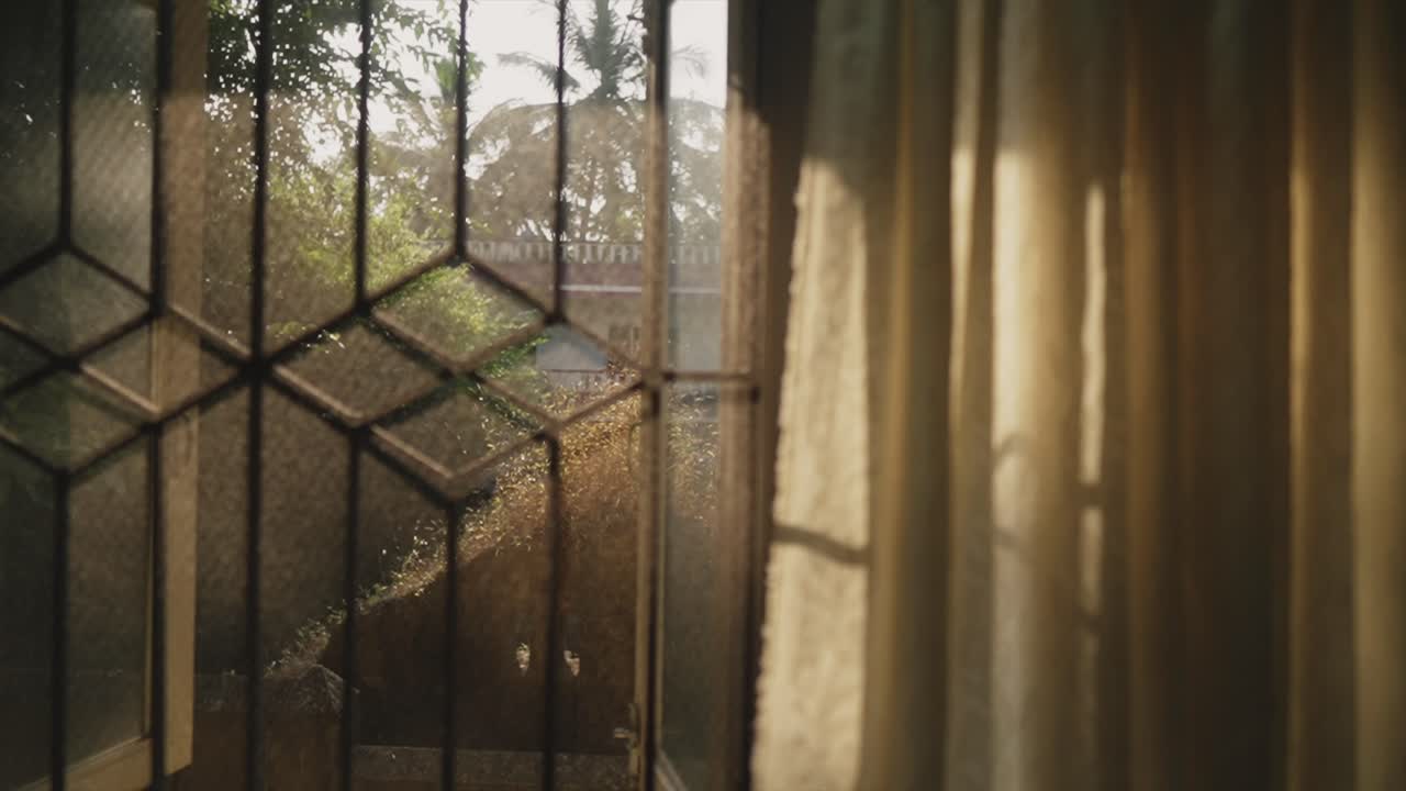 Cinematic shot of early morning sun rays shining and peaking through the curtains of this window