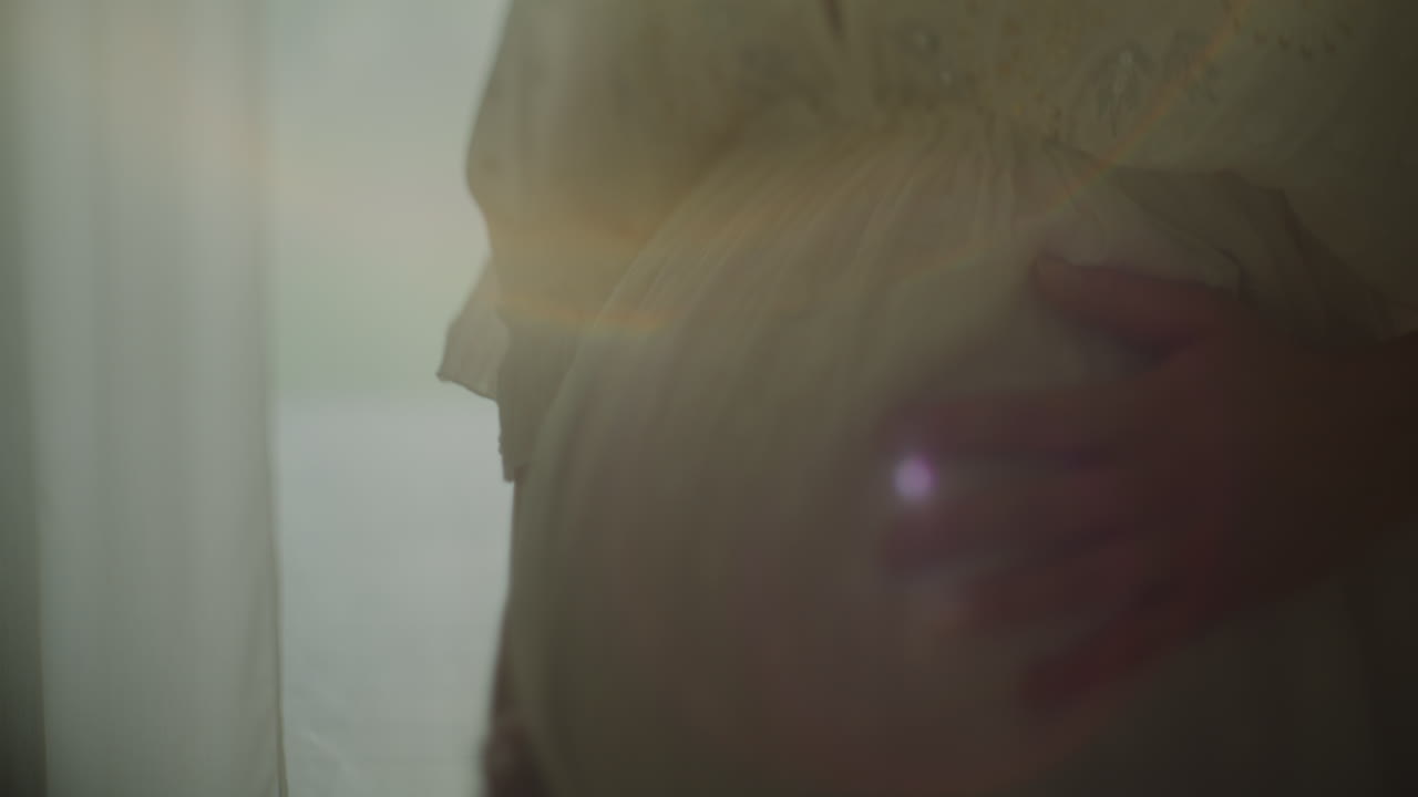 Close-up of Pregnant Woman's Belly in Sunlight Near Window