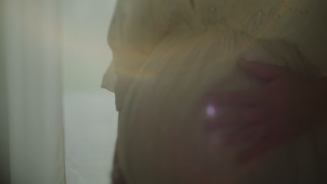close-up of pregnant woman's belly in sunlight near window