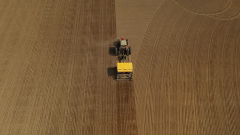 seguimiento de la vista aérea de un tractor rojo de dos ruedas sembrando semillas en línea recta en un campo agrícola con una sembradora amarilla durante la primavera