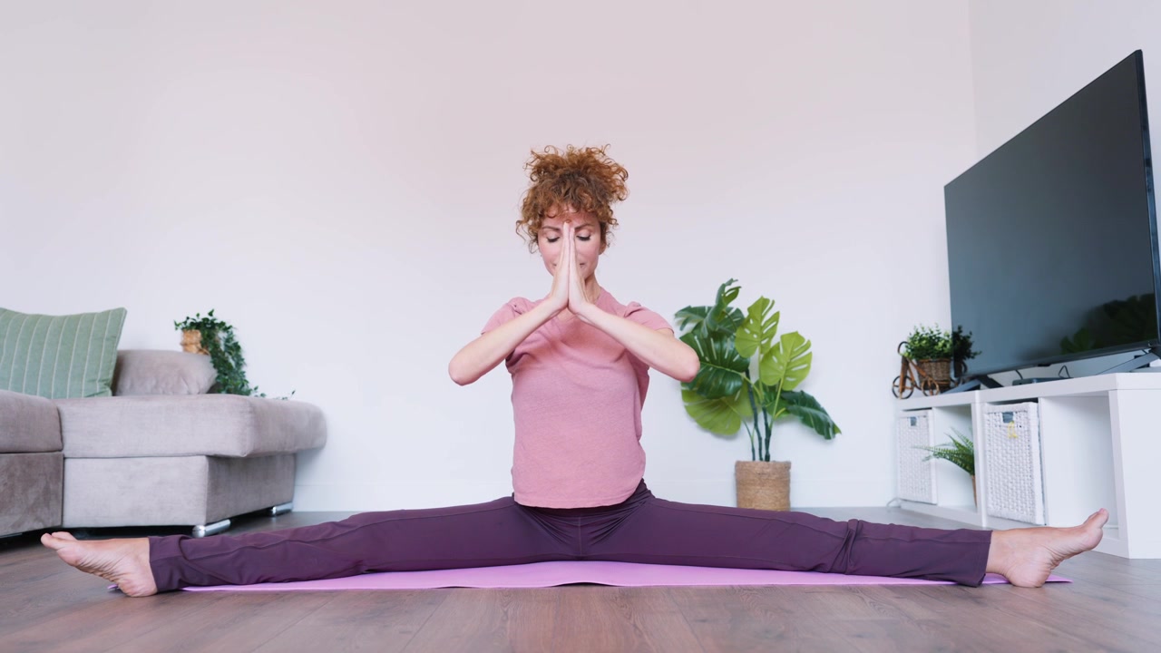 Mulher praticando a postura de yoga da flexão sentada para frente com as pernas afastadas em casa.