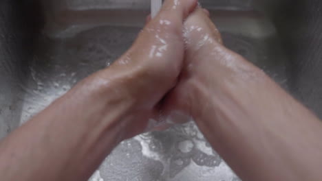 closeup of a person's hand washing with soap under clean tap water from a faucet - high-angle shot