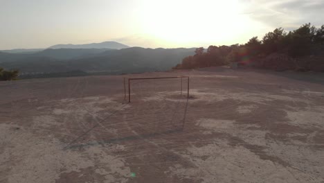 aerial: empty football or soccer goal on hard ground pitch at sunset