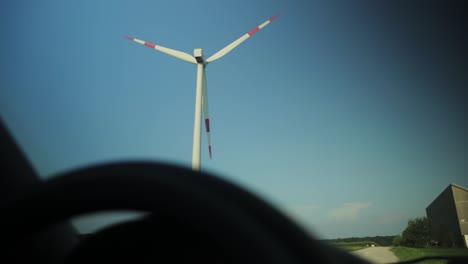 looking out of a car at a spinning windmill on a sunny afternoon