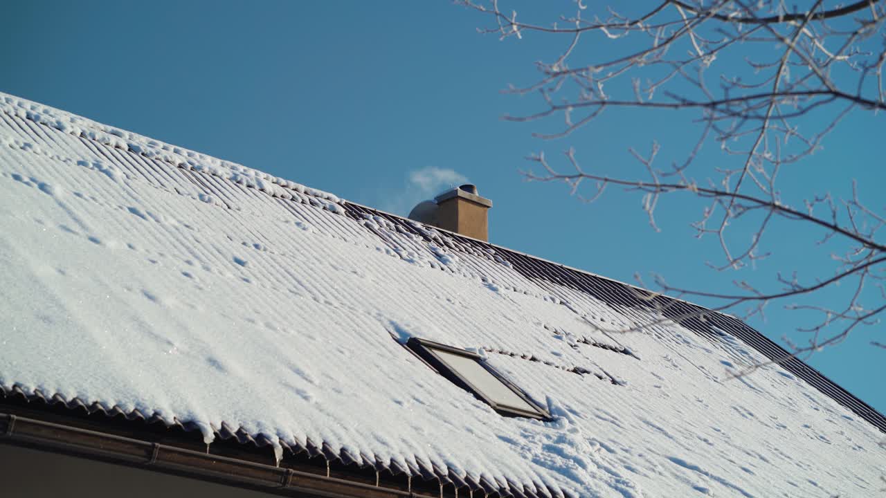White smoke coming out of a chimney in winter. Roof covered with snow. Keeping home warm.