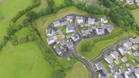 Drone-view-of-rural-development-of-new-build-homes-in-the-UK-countryside,-showcasing-modern-residential-buildings-amidst-green-fields