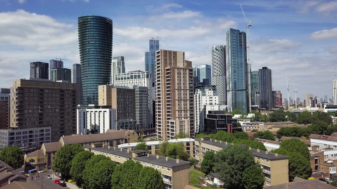 Aerial drone view of getting closer to the buildings in Canary Wharf London over the residential houses on a scattered cloudy day