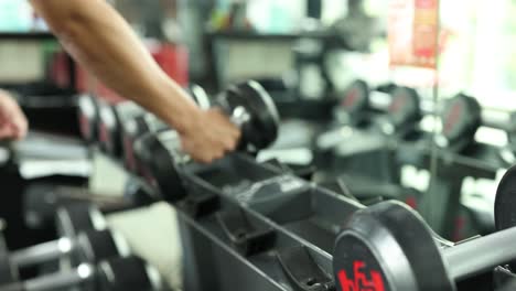 A person selects and lifts dumbbells in a well-lit gym environment, focusing on strength training exercises