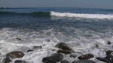 waves washing over small smooth rocks on the beach