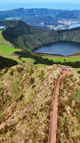 following a female tourist walking by the road leading to the mountain top. aerial perspective on the spectacular nature of the azores. vertical video.