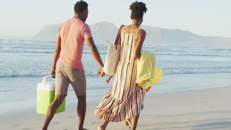 happy african american couple walking with daughter and son on sunny beach