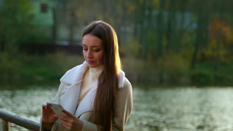 woman using smartphone by a lake in an autumn park