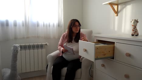 pregnant woman in baby room writing checklist, planning for newborn arrival. pan right