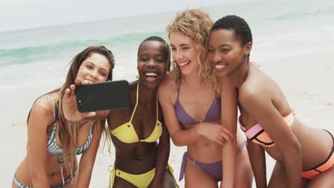 vista frontal de amigas de raza mixta tomando selfies con teléfono móvil en la playa 4k