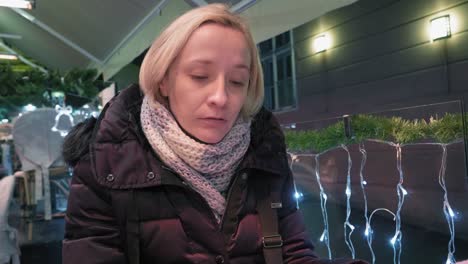 woman eating in cafe, outdoors on terrace, turning away, talking - christmas lights all around