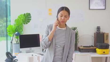 Architektin,-Die-Im-Büro-Arbeitet-Und-Am-Schreibtisch-Steht-Und-Mit-Dem-Mobiltelefon-Spricht