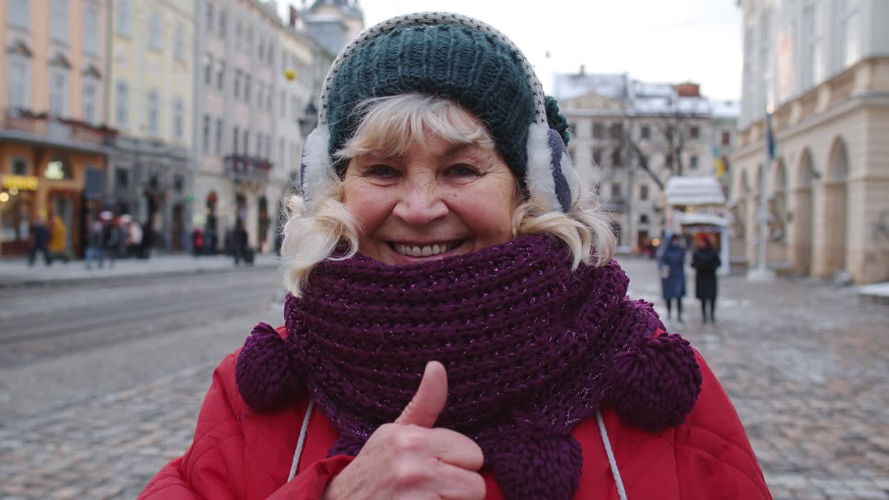 una turista anciana y elegante sonriendo, mostrando el pulgar hacia arriba en el centro de la ciudad invernal de lviv, ucrania