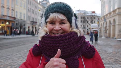 Stylish-old-senior-woman-tourist-smiling,-showing-thumb-up-in-winter-city-center-of-Lviv,-Ukraine