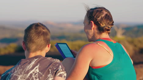 woman and child reading an e-reader outdoors with a scenic view