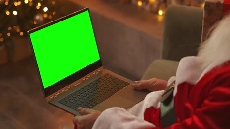 Papá-Noel-Está-Hablando-En-Una-Videollamada-A-Través-De-Una-Computadora-Portátil.-Utilice-La-Pantalla-Verde-Para-Una-Videollamada.-Papá-Noel-Saluda-Con-La-Mano-Mirando-La-Pantalla-Verde-Del-Portátil.-Imágenes-4k-De-Alta-Calidad