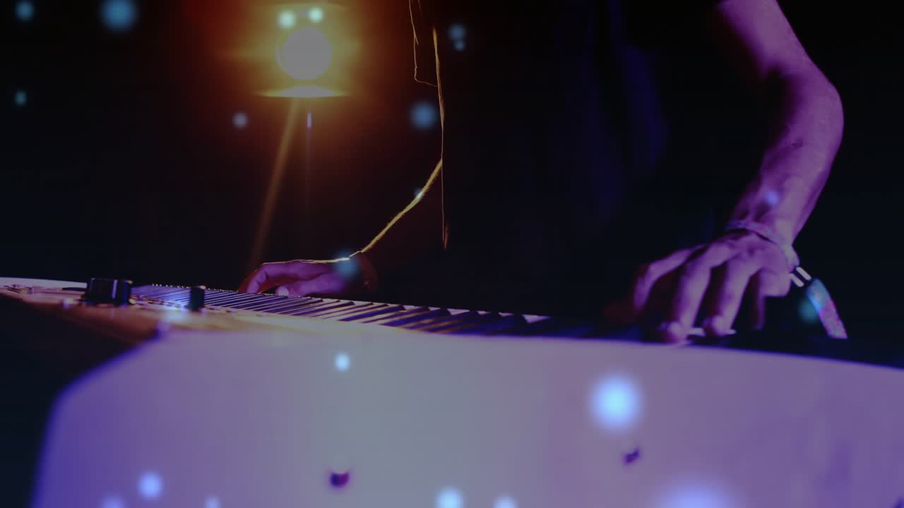 Musician pressing keys and tweaking synth camera rising, blue particles around hands shaping music