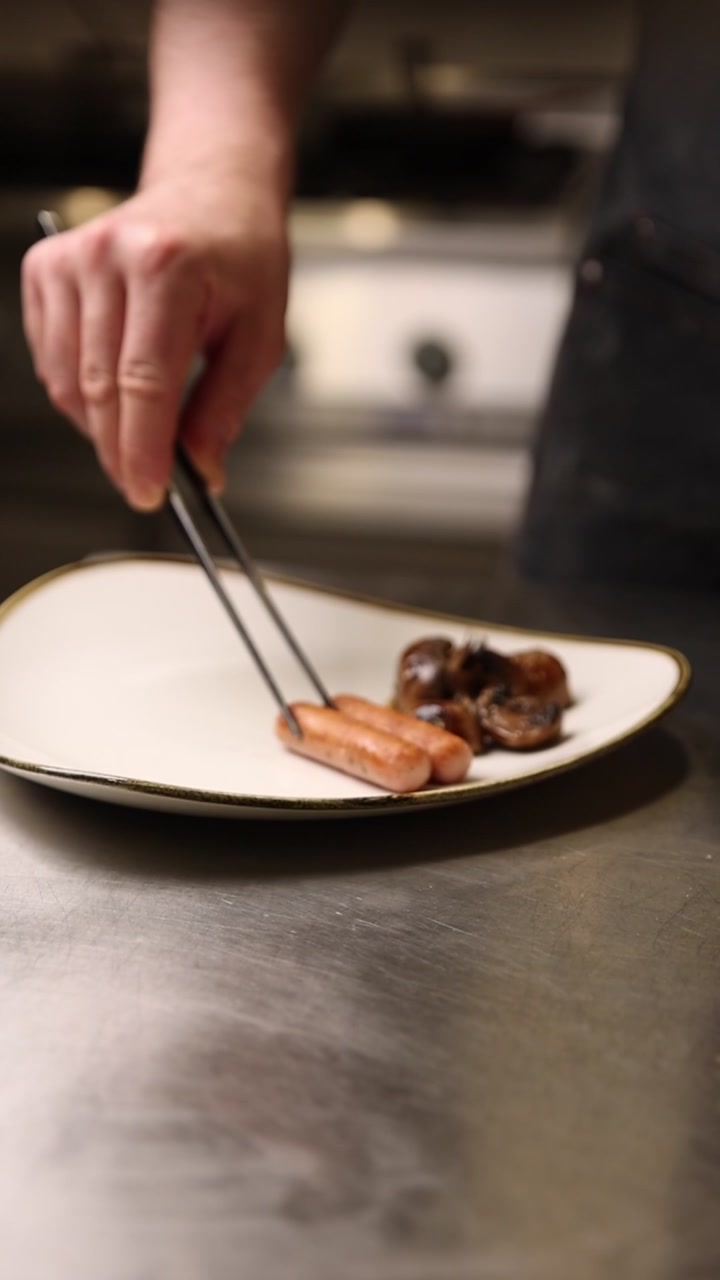 Close-up of a Chef Plating Sausages and Mushrooms with Tongs