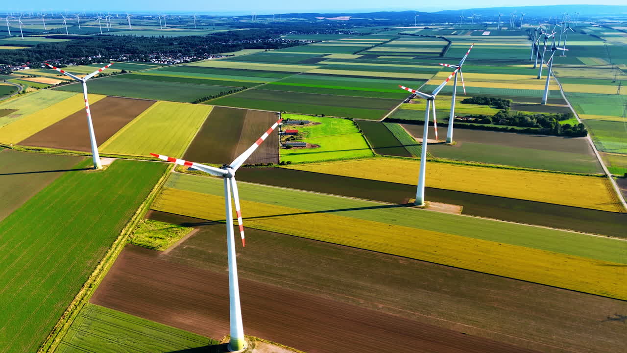 Green, yellow and brown patches of fields with windmills. Aerial perspective on the rural area with wind farms.