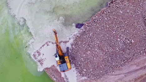 birdseye view areal shot of a industrial loader digging for sand in the ocean and putting on the beach