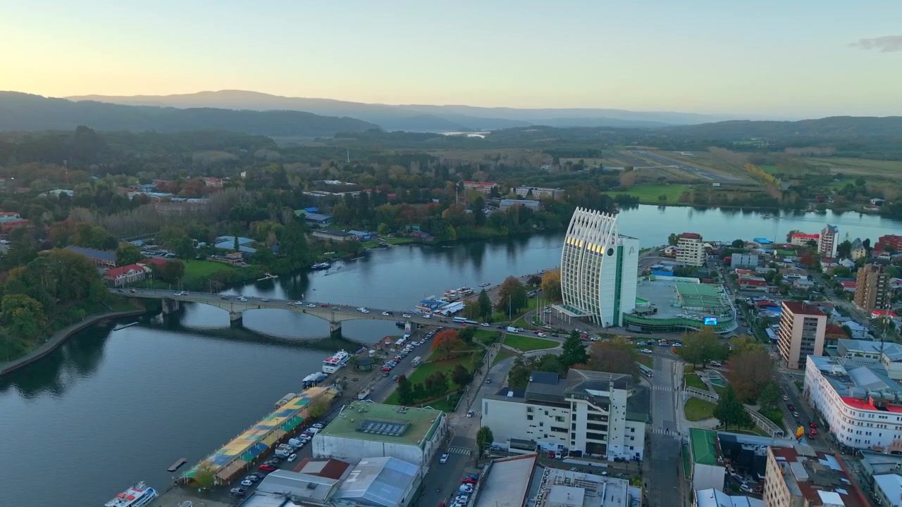 Panoraamailmakuva Valdivian keskustasta, Chilestä, Pedro de Valdivia -sillan kanssa auringonnousun aikaan, vuorten ympäröimänä ja Las Mariasin lentokenttä taustalla