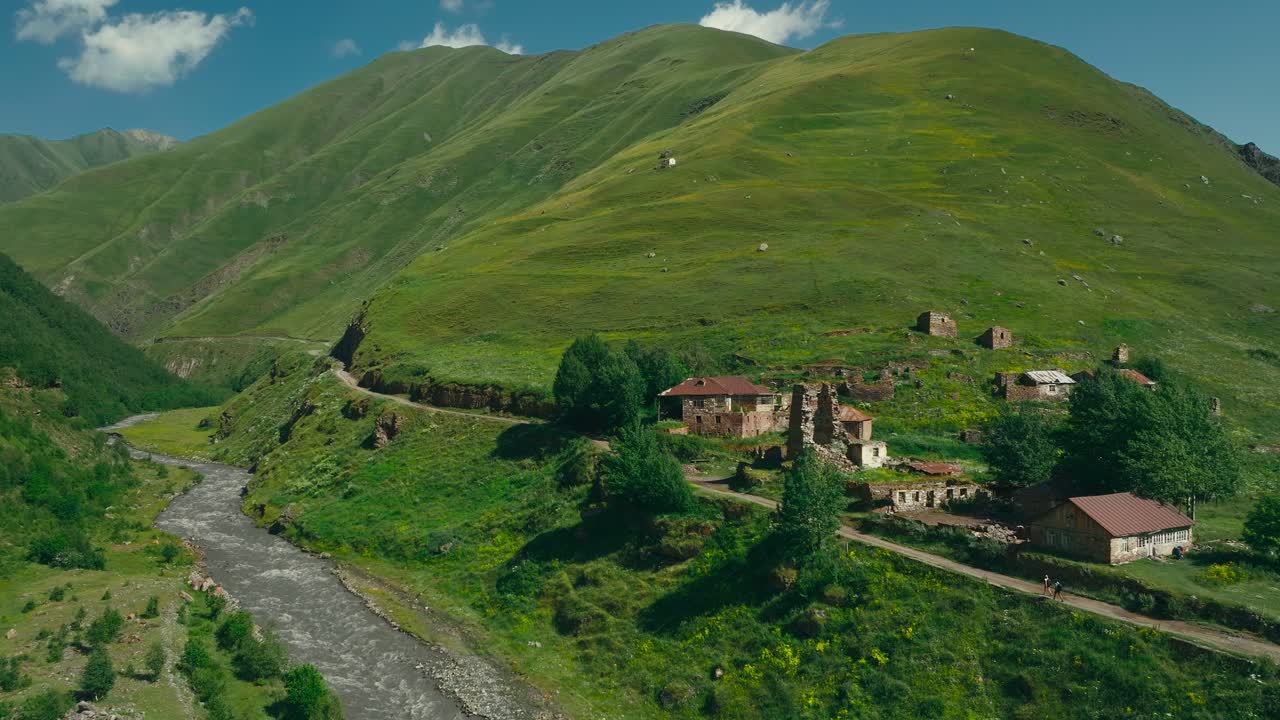 Caminhantes percorrem ruínas abandonadas numa pitoresca e exuberante paisagem montanhosa verde, com um rio a correr no vale, na Geórgia