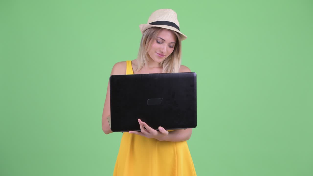 fotografía de estudio de una joven turista sonriendo y pensando mientras usa una computadora portátil contra un fondo verde
