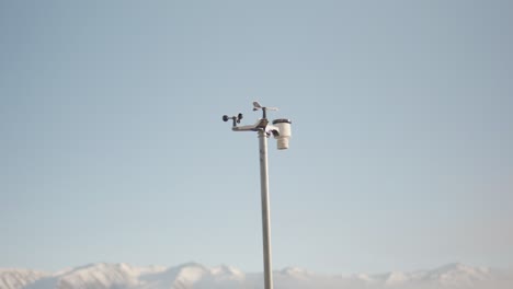 estación meteorológica inalámbrica montada en un poste frente a montañas cubiertas de nieve