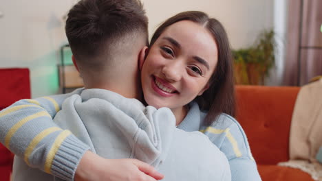 Portrait-of-woman-embracing,-hugging-man,-looking-at-camera-over-his-shoulder-at-home-room,-support