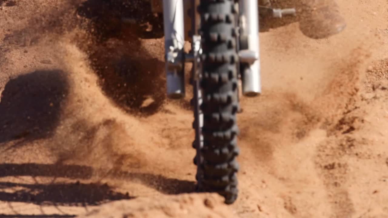 Close-up of a motorcycle tire navigating through loose sand, showcasing the challenge of maintaining traction.