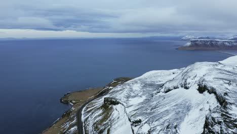 drone flying above snow-covered mountain surrounded by cold blue ocean