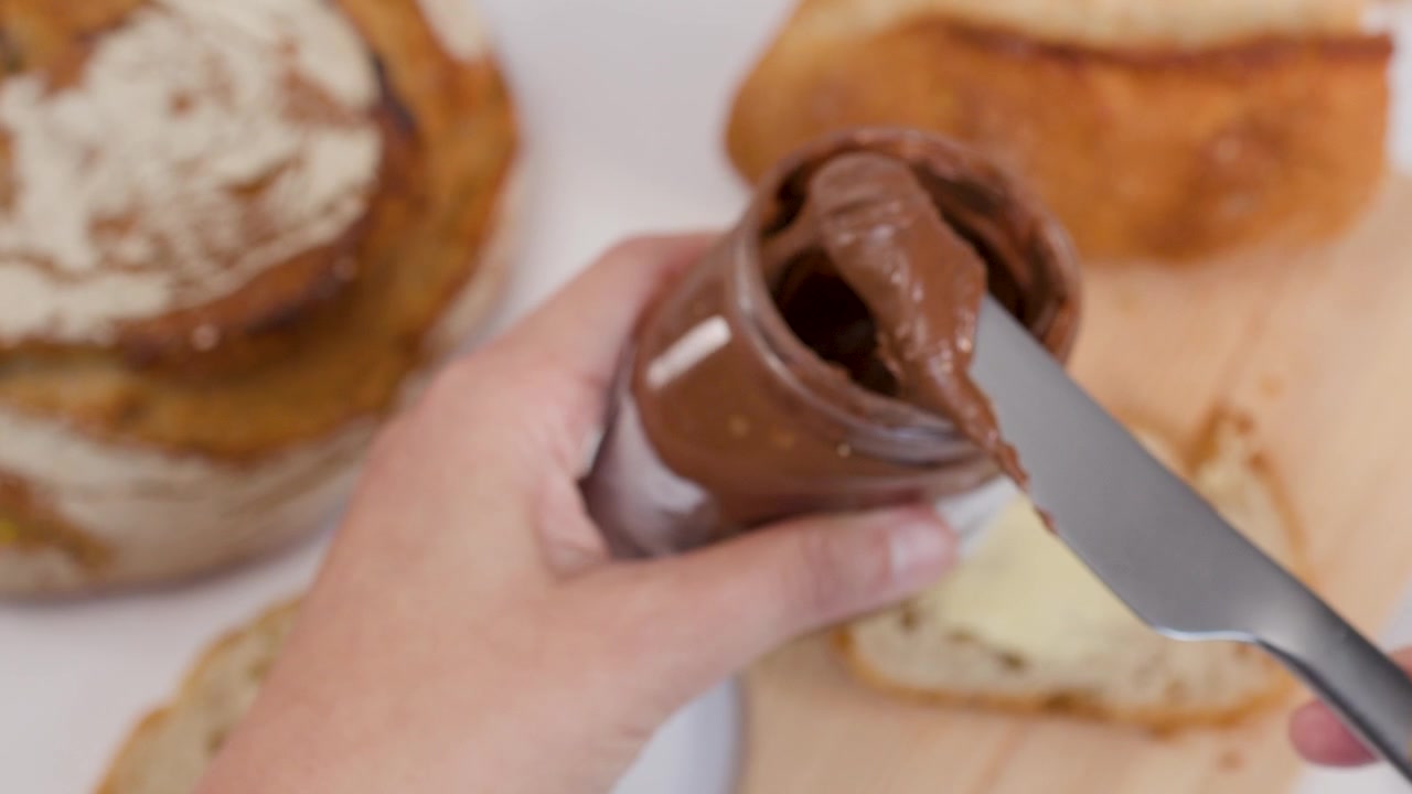 Ripresa ravvicinata dall'alto di mani che prelevano crema al cioccolato da un barattolo su pane croccante