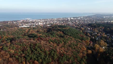 Scenic-aerial-panorama-of-autumn-forest-by-Sopot-city-and-Bay-of-Gdansk,-Poland