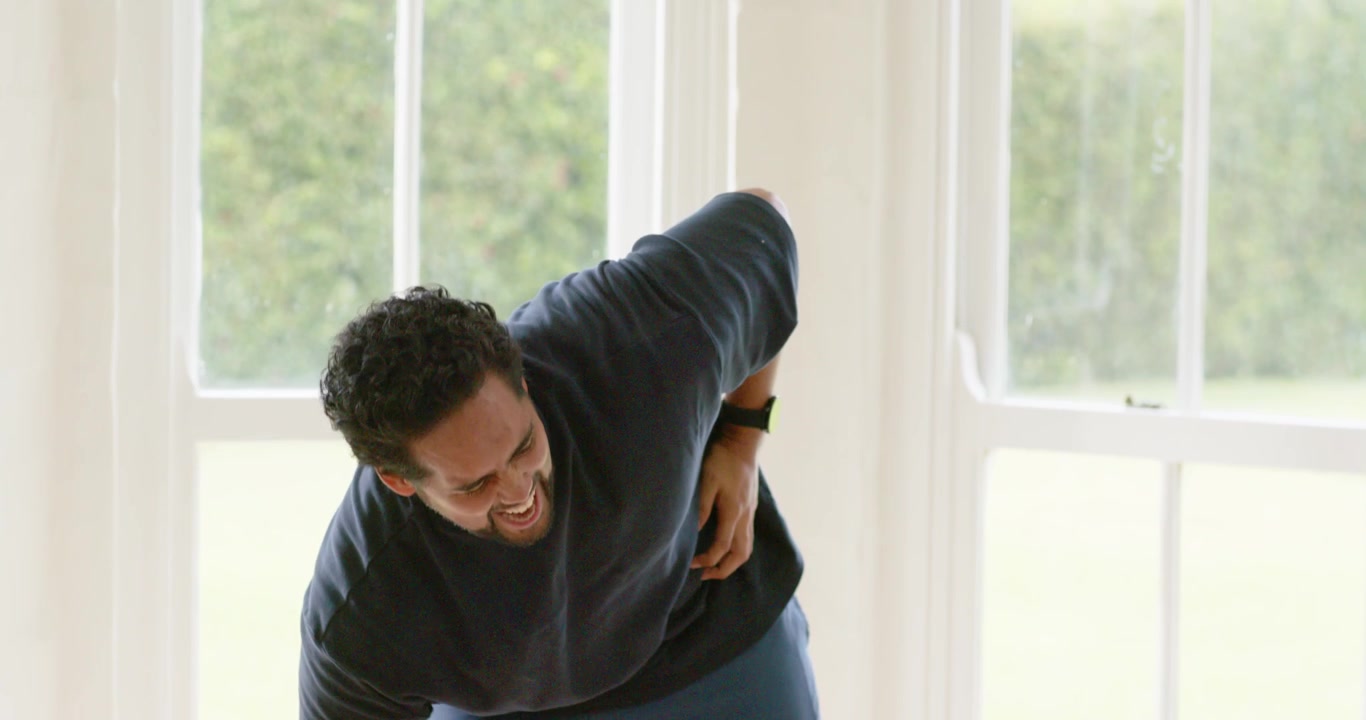 African American man lowering weight bending and pressing right flank in windowed room easing cramp