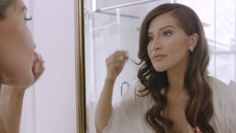 bride looking in the mirror, putting on wedding day earrings