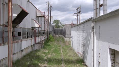 Imágenes-De-Drones-Empujando-Hacia-Adelante-Sobre-Vías-De-Ferrocarril-Cubiertas-De-Maleza-En-Una-Fábrica-Abandonada