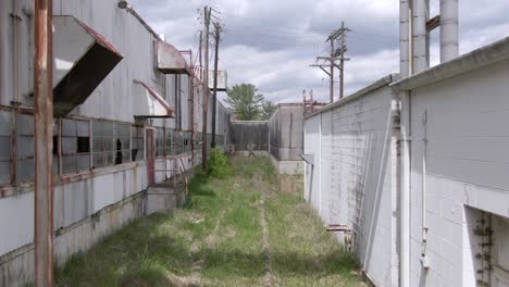 imágenes de drones empujando hacia adelante sobre vías de ferrocarril cubiertas de maleza en una fábrica abandonada