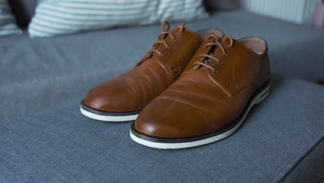 A-pair-of-stylish-brown-leather-shoes-are-neatly-placed-on-a-gray-couch