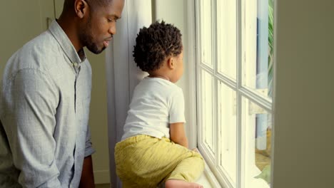 Seitenansicht-Eines-Jungen-Schwarzen-Vaters,-Der-Mit-Seinem-Sohn-Auf-Der-Fensterbank-In-Einem-Komfortablen-Zuhause-Spielt,-4K