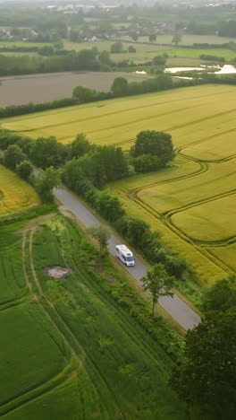vertical drone shot tracking a rv driving in middle of canola fields, sunset