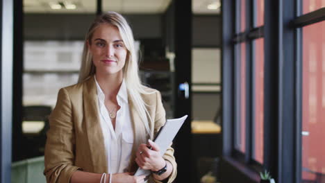 millennial white blonde businesswoman holding documents, turns and smiles to camera, close up